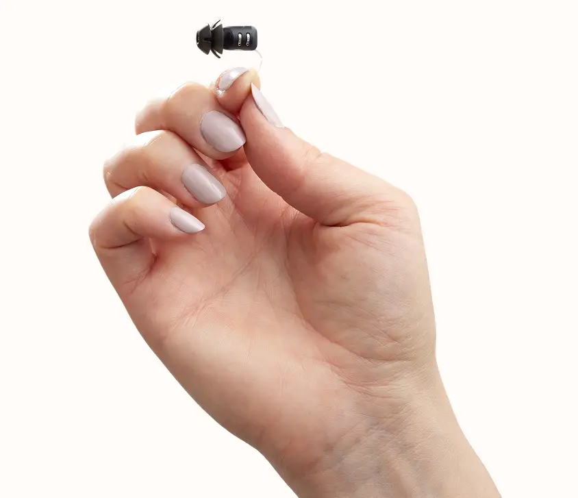 Eargo virtually invisible hearing aid held between fingertips