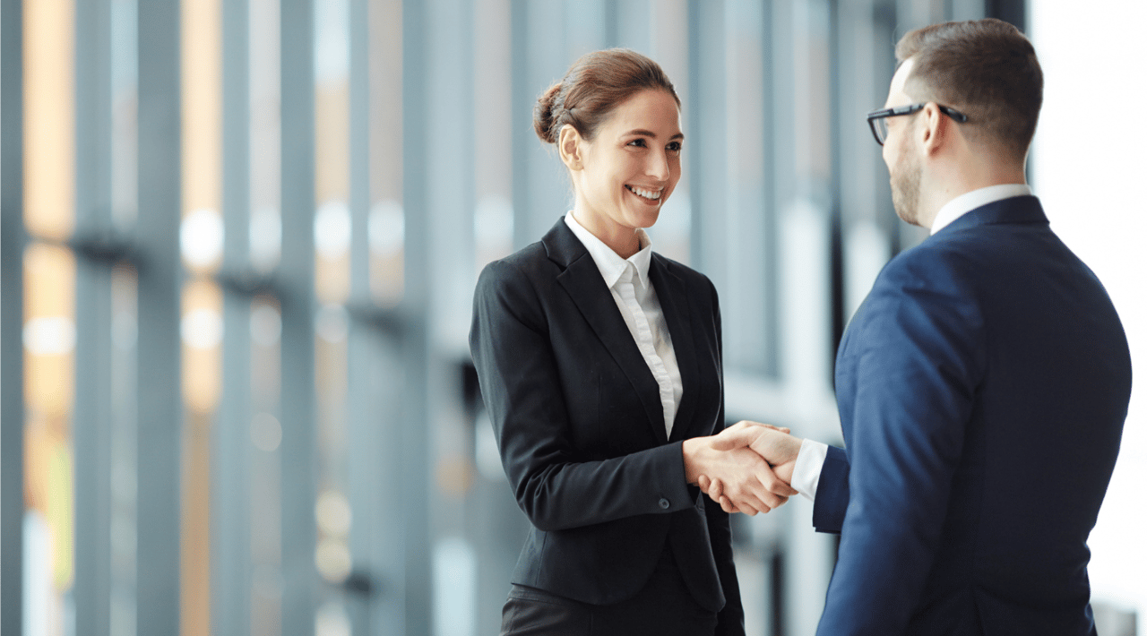 Picture of sharply dressed woman and man shaking heads on a blurry background.