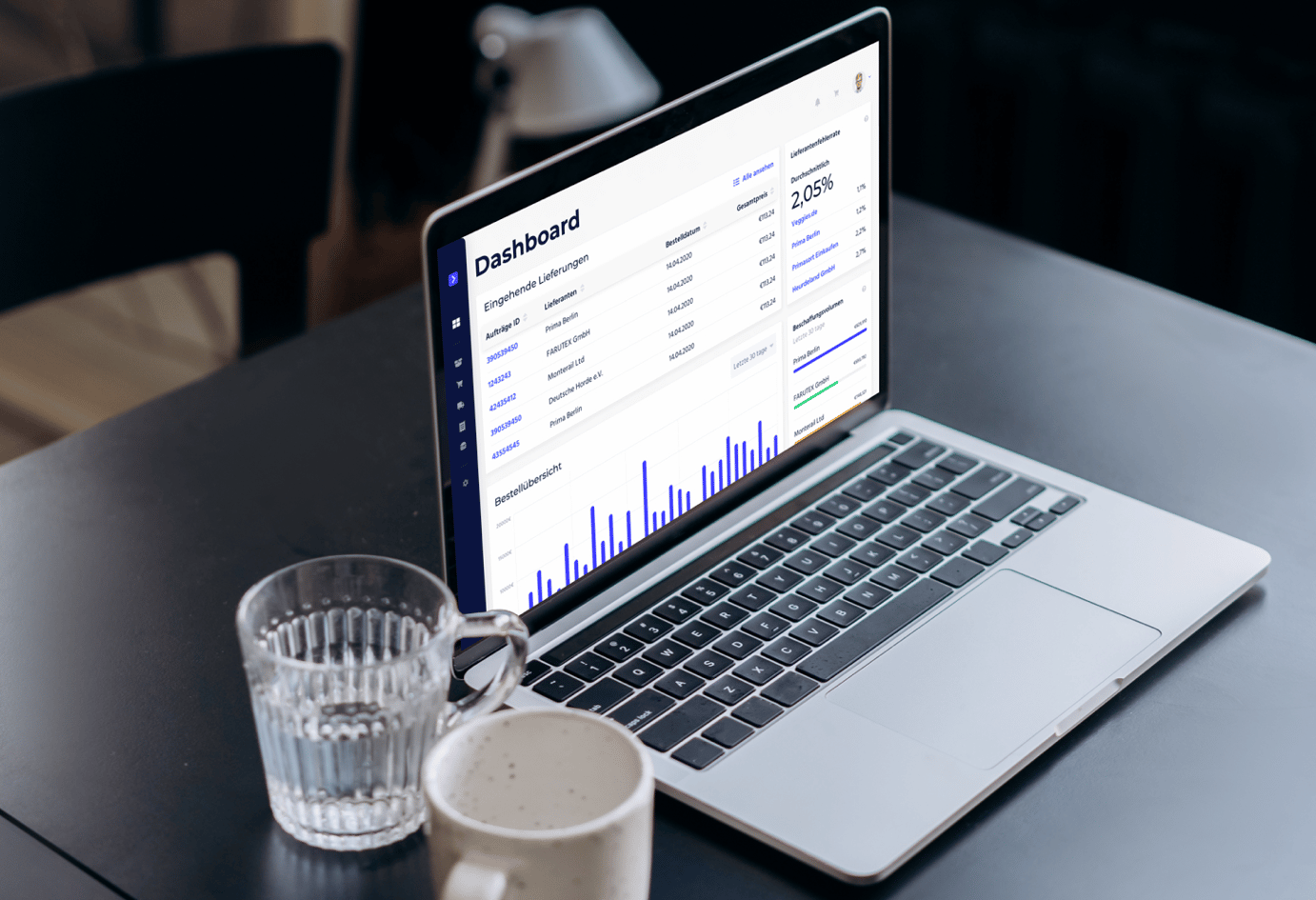 Picture of grey laptop on a black desk, with a cup and a glass standing beside it. On the laptop screen there is a view from the Avisio hotel inventory management application built by Monterail.