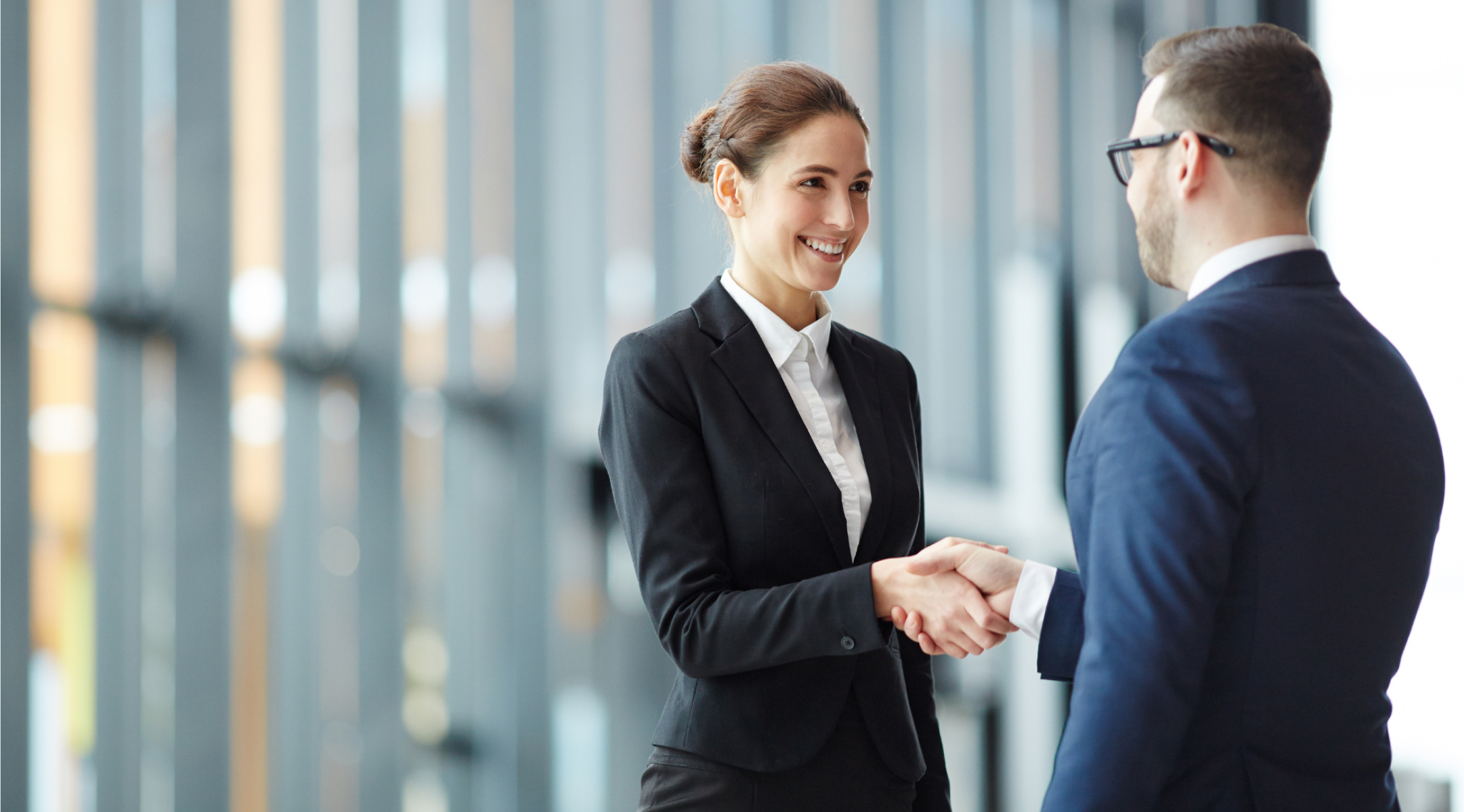 Picture of sharply dressed woman and man shaking heads on a blurry background.