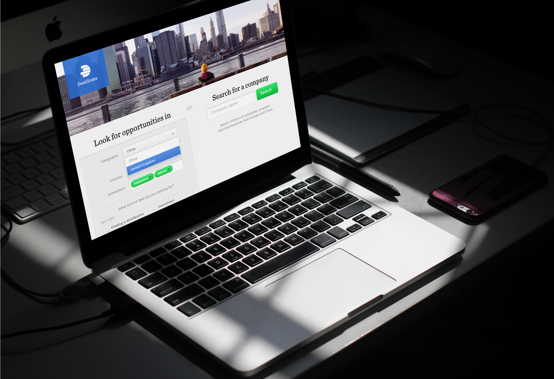 Picture of laptop on a grey desk in a shadowy surrounding. On the laptop screen is a view from the DealGlobe platform developed by Monterail.